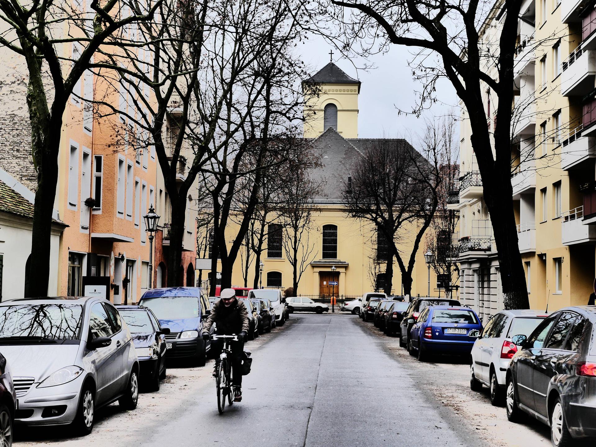 Aufnahme der winterlichen Luisenkirche in Berlin. Auf der Straße davor stehen Autos. Ein Rafahrer fährt in Richtung der Kamera.