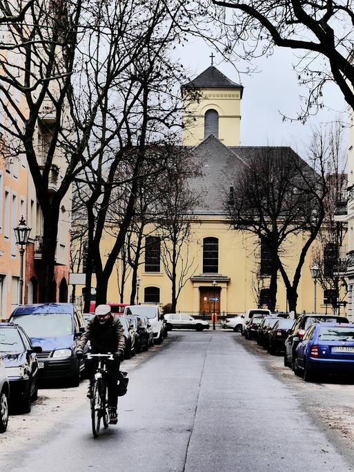 Aufnahme der winterlichen Luisenkirche in Berlin. Auf der Straße davor stehen Autos. Ein Rafahrer fährt in Richtung der Kamera.