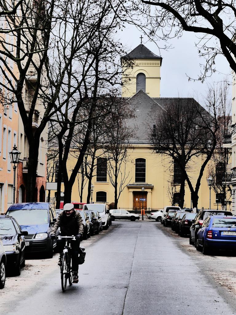 Aufnahme der winterlichen Luisenkirche in Berlin. Auf der Straße davor stehen Autos. Ein Rafahrer fährt in Richtung der Kamera.