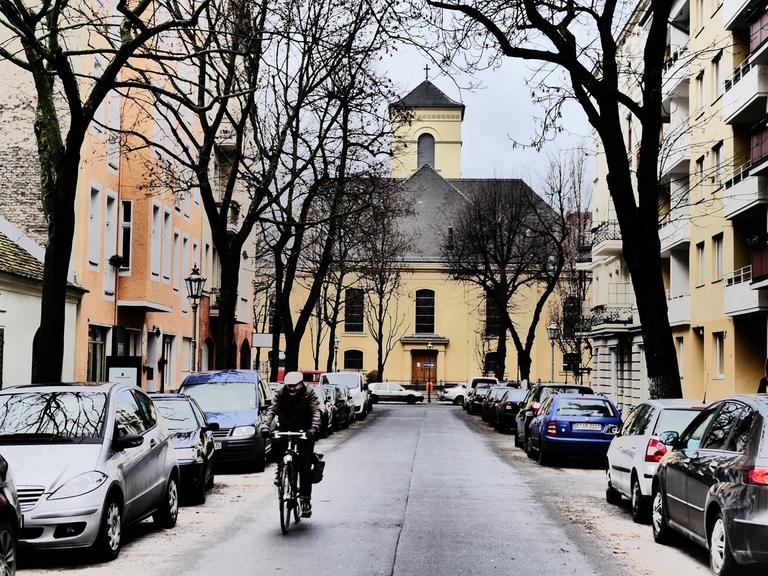 Aufnahme der winterlichen Luisenkirche in Berlin. Auf der Straße davor stehen Autos. Ein Rafahrer fährt in Richtung der Kamera.