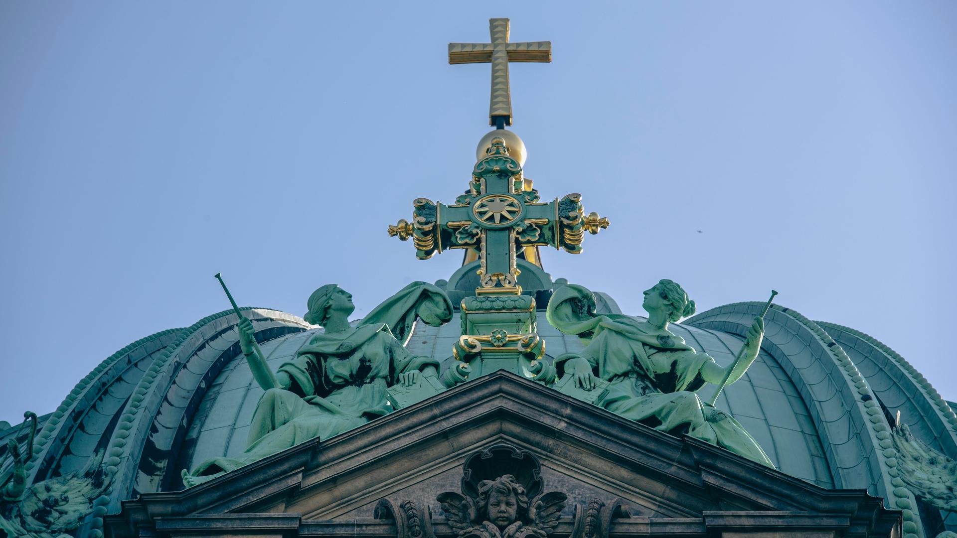 Das Kreuz auf dem Dach des Berliner Doms leuchtet im Licht der Sonne.