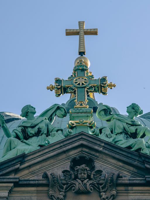 Das Kreuz auf dem Dach des Berliner Doms leuchtet im Licht der Sonne.