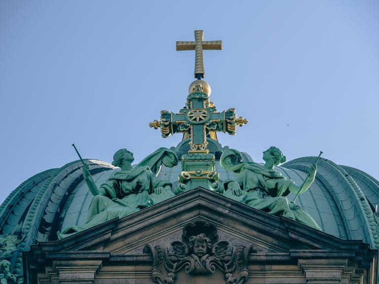 Das Kreuz auf dem Dach des Berliner Doms leuchtet im Licht der Sonne.