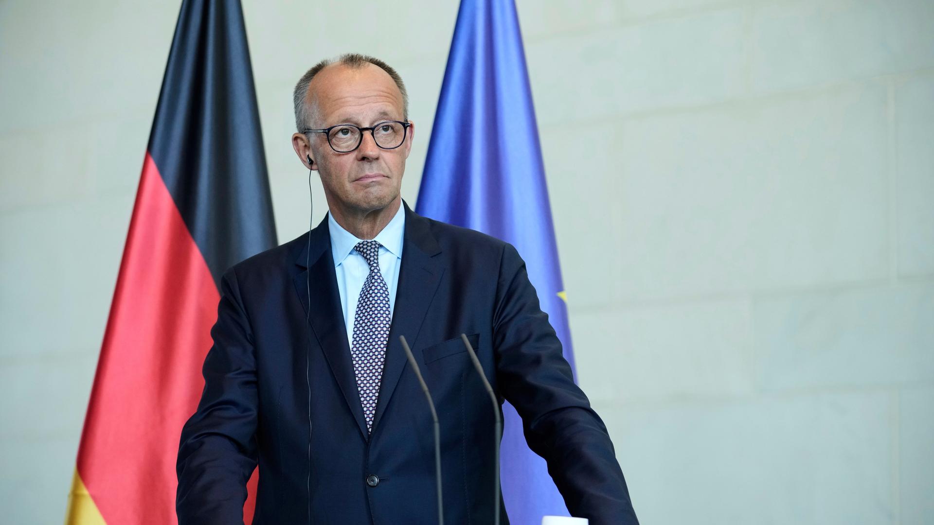 Bundeskanzler Friedrich Merz spricht in Berlin. Im Hintergrund sind die deutsche und europäische Flagge. 