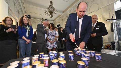 Brüssels Bürgermeister Philippe Close zündet eine von vielen Kerzen an, die auf einem Tisch im Jüdischen Museum in Brüssel stehen. Hinter ihm stehen noch andere Teilnehmer.