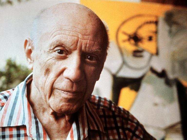 Der Maler Pablo Picasso blickt in die Kamera, im Hintergrund ein Gemälde von ihm. (Quelle: dpa)