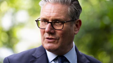 Der britische Premier Keir Starmer mit Brille, grauen Haaren und in Anzug spricht im Freien zur Seite