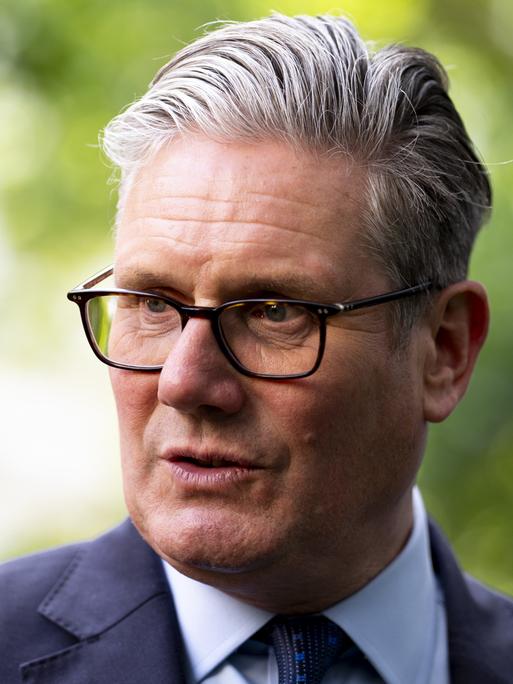 Der britische Premier Keir Starmer mit Brille, grauen Haaren und in Anzug spricht im Freien zur Seite