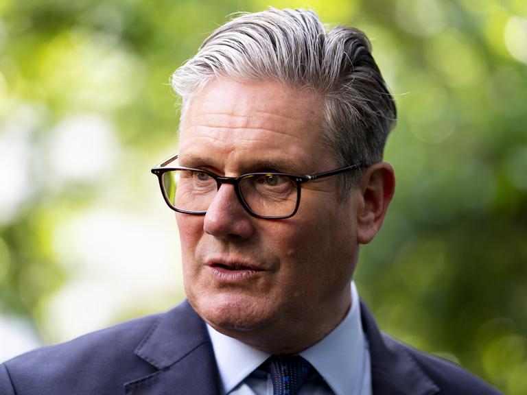 Der britische Premier Keir Starmer mit Brille, grauen Haaren und in Anzug spricht im Freien zur Seite Der britische Premier Keir Starmer mit Brille, grauen Haaren und in Anzug spricht im Freien zur Seite
