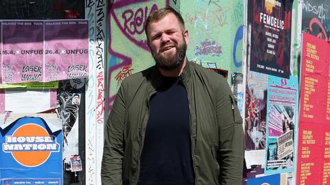 Jan "Monchi" Gorkow, Sänger und Frontmann der Band Feine Sahne Fischfilet, steht  vor eine Tür eines Hauses.  An dem Haus sind viele Plakate geklebt.