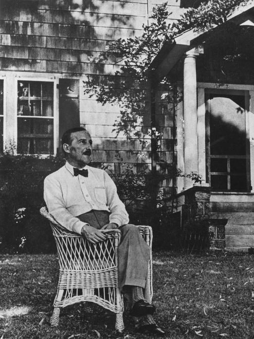 Stefan Zweig sitzt im Vorgarten eines Gebäudes in einem Korbstuhl.