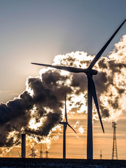 Windkraftanlagen vor einem Kohlekraftwerk, vor einem orangenen Sonnenuntergang.