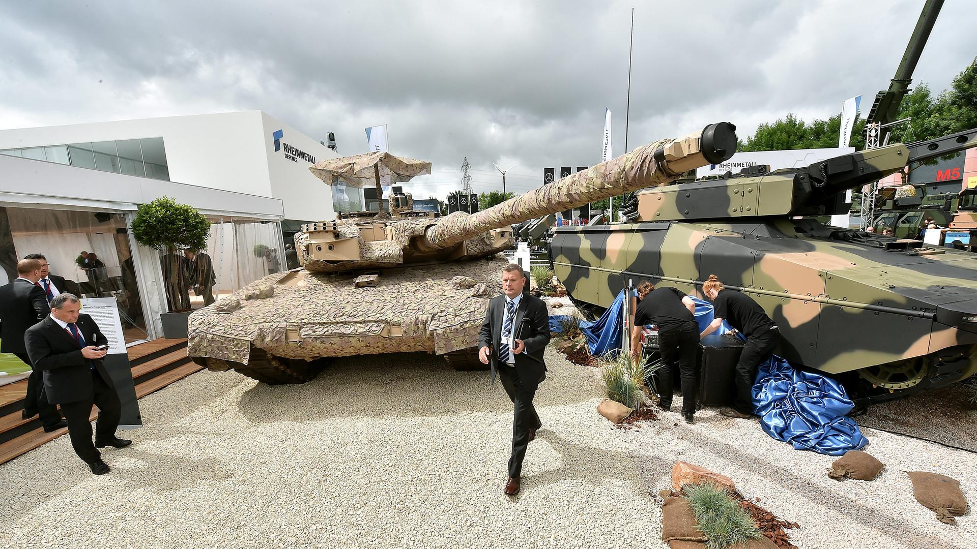 Männer in Anzügen und Reinigungspersonal vor Panzern auf der Rüstungsmesse Eurosatory in Paris.