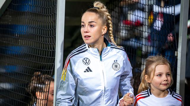 Giulia Gwinn betritt ein Stadion. Sie hält ein Ballmädchen an der Hand.