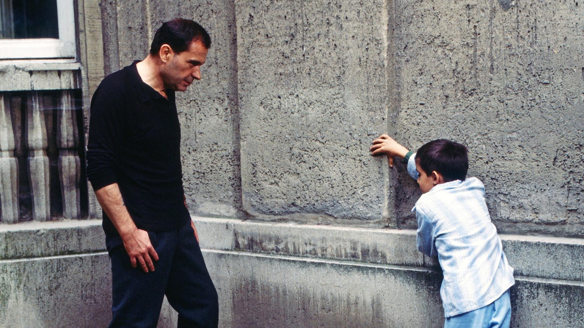 Ein Mann und ein Junge stehen sich gegenüber und lehnen an einer Wand. Eine Szene aus dem Film "Der Boxer".