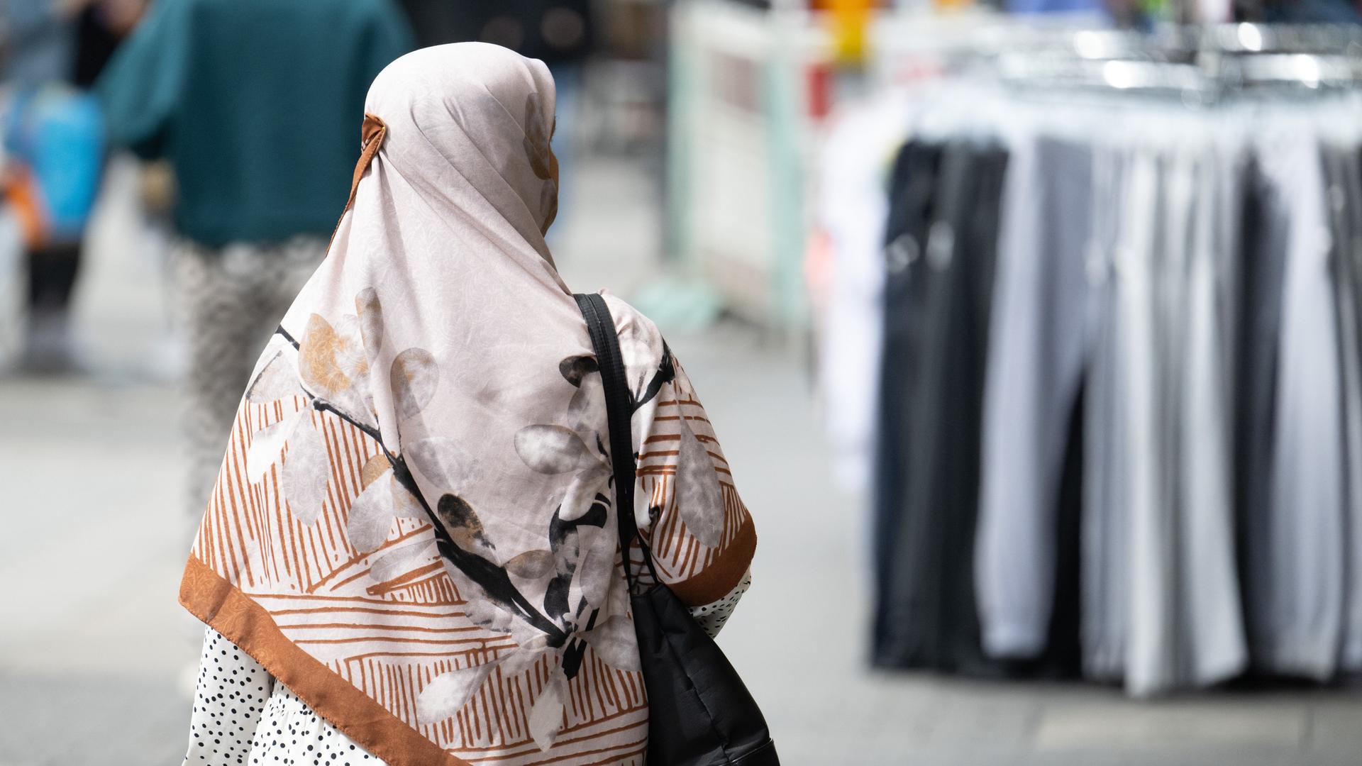 Eine Frau mit einem Kopftuch, die von hinten fotografiert ist, geht durch die Fußgängerzone von Offenbach. 
