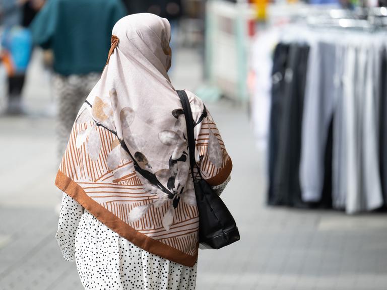 Eine Frau mit einem Kopftuch, die von hinten fotografiert ist, geht durch die Fußgängerzone von Offenbach. 