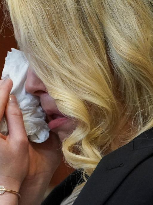 Nahaufnahme von Amber Heard im Gerichtssaal, die sich, halb von ihrem blonden Haar verborgen, Tränen mit einem Taschentuch abwischt.
