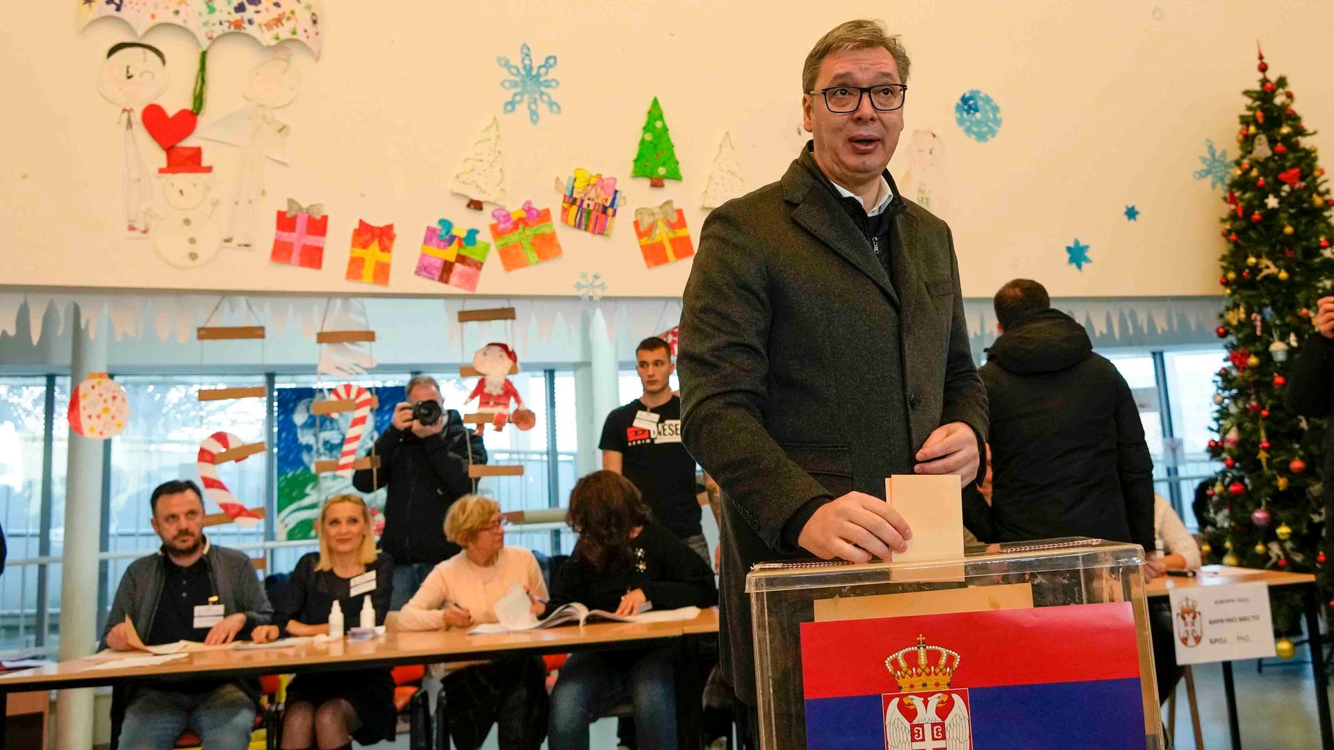 Der serbische Präsident Vucic steht in einem Wahllokal in Belgrad vor einer Urne und hält einen Stimmzettel in der Hand. Der serbische Präsident Vucic steht in einem Wahllokal in Belgrad vor einer Urne und hält einen Stimmzettel in der Hand.