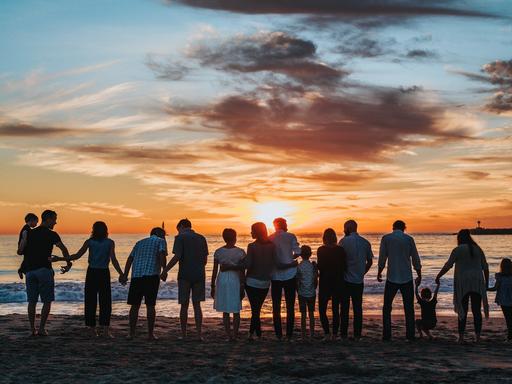 Eine große Familie steht am Strand und hält sich an den Händen, während sie den Sonnenuntergang betrachten. 