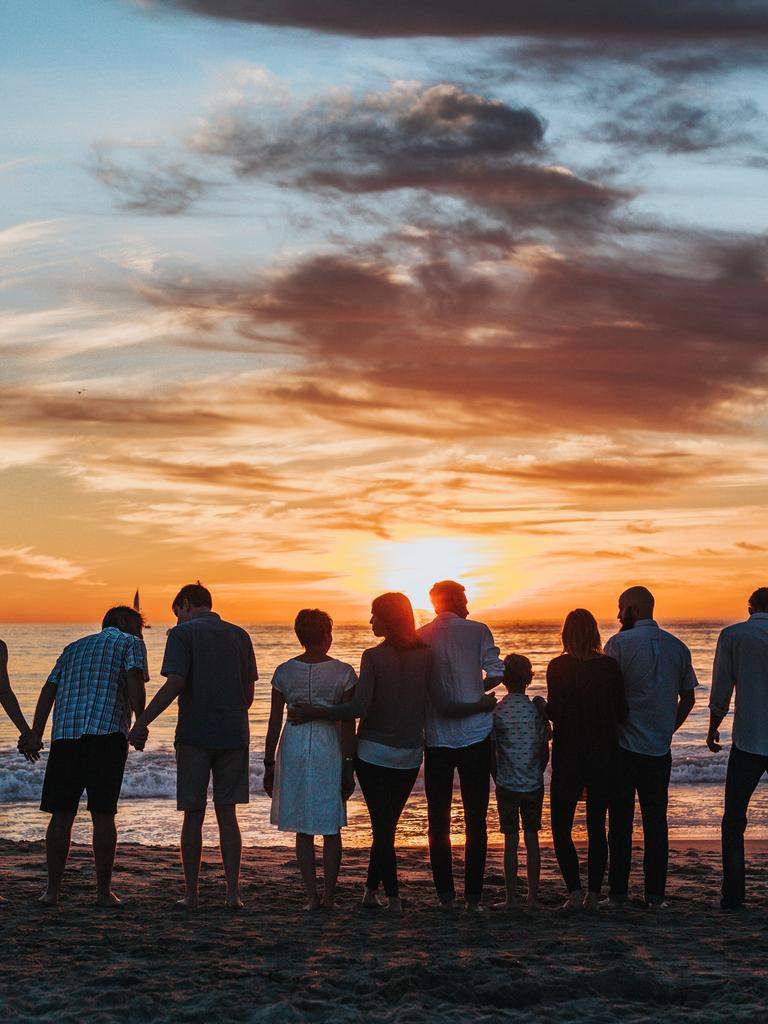 Eine große Familie steht am Strand und hält sich an den Händen, während sie den Sonnenuntergang betrachten. 