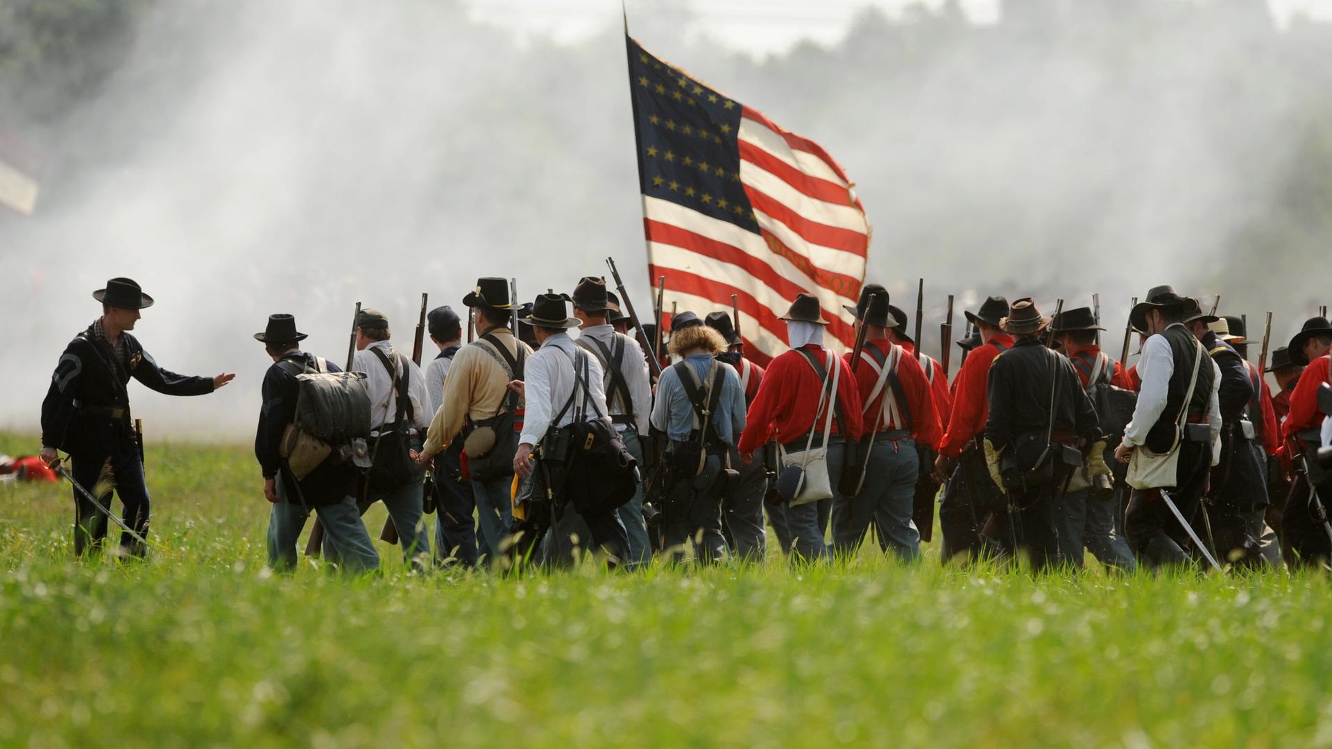 Ein Reenactment des Amerikanischen Bürgerkriegs auf einer Wiese. Eine Gruppe von Männern läuft dicht gedrängt, in der Mitte der Gruppe trägt einer die US-Flagge.