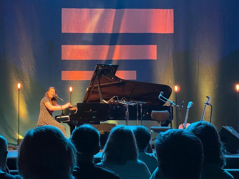 Michelle Willis sitzt am Flügel im Kammermusiksaal vor dem Streifenlogo von Deutschlandfunk.
