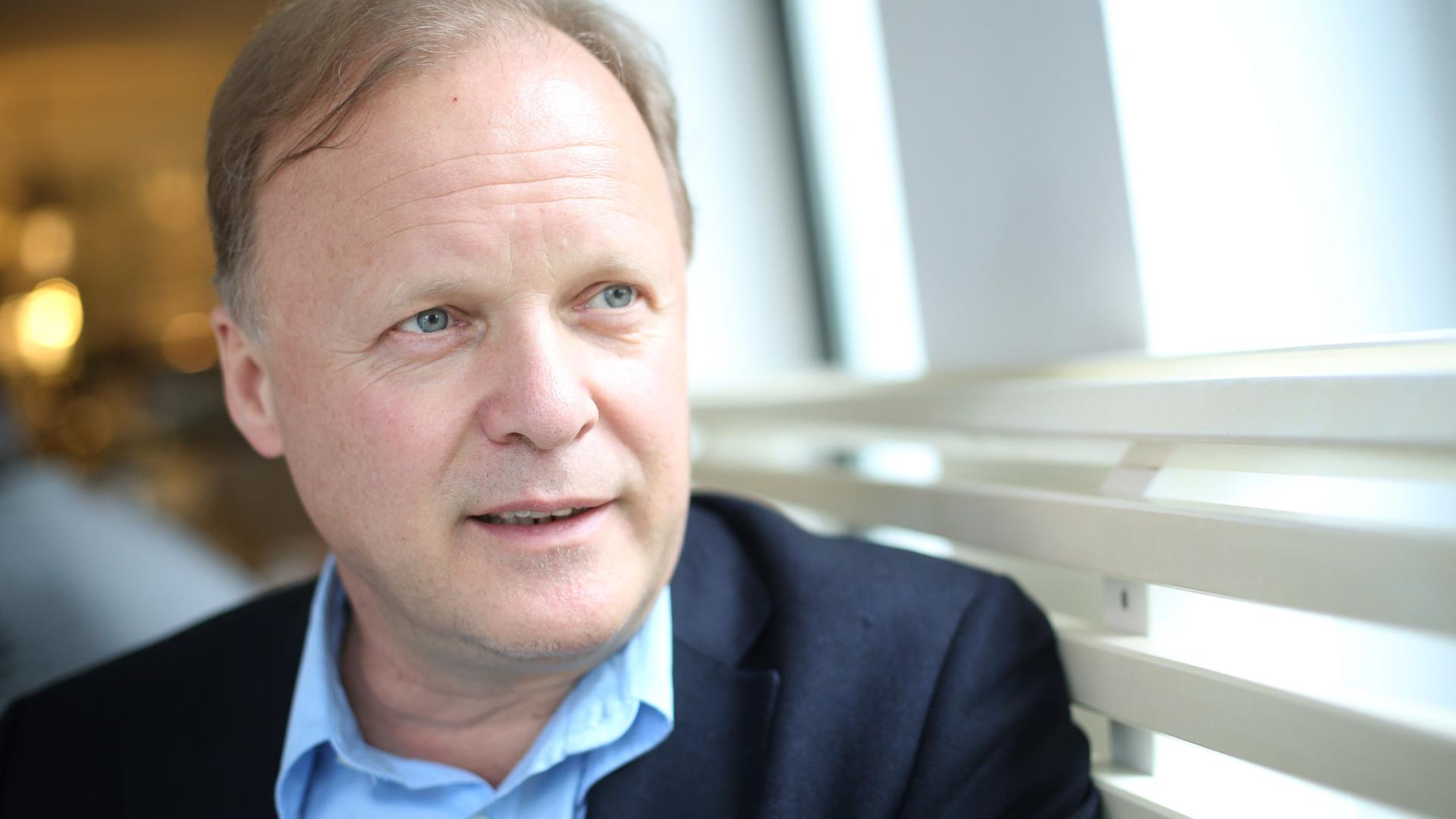 Stephan Werhahn sitzt auf einer Bank in einem Café und schaut aus dem Fenster. Er trägt ein hellblaues Hemd zum dunkelblauen Anzug. Stephan Werhahn sitzt auf einer Bank in einem Café und schaut aus dem Fenster. Er trägt ein hellblaues Hemd zum dunkelblauen Anzug.