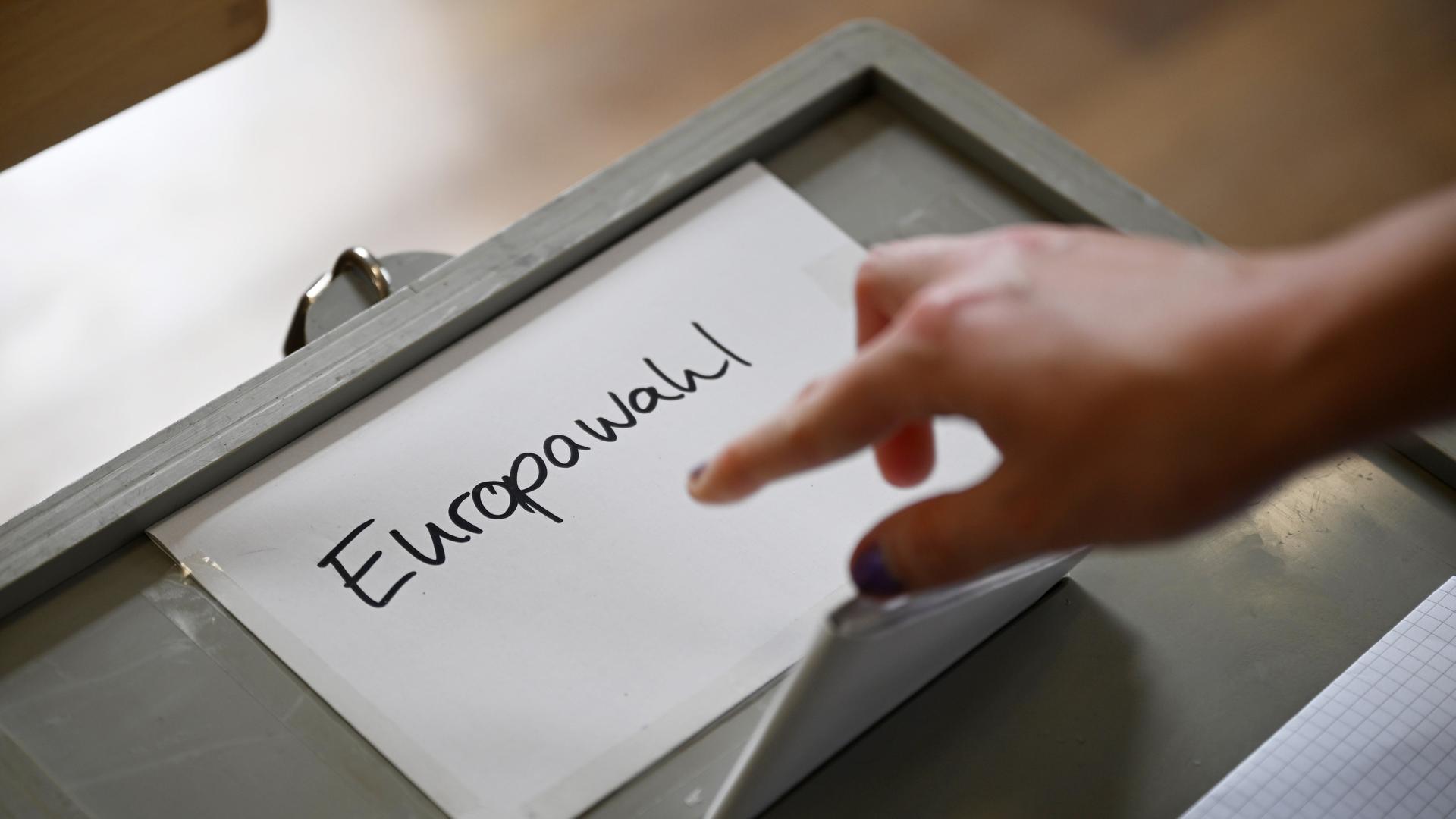 Auf einer Wahlurne steht "Europawahl". Ein Hand schmeißt einen Wahlzettel in die Urne.