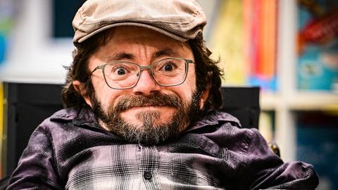 Raúl Krauthausen trägt Mütze und blickt lächelnd in die Kamera