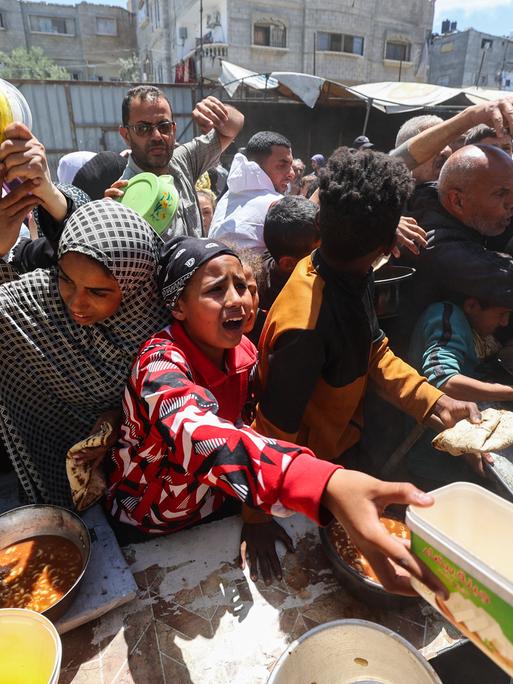 Palästinenser stehen für eine warme Mahlzeit in einer vom Welternährungsprogramm der Vereinten Nationen (WFP) betriebenen Küche im Flüchtlingslager Nuseirat im zentralen Gazastreifen an, 26. April 2025.