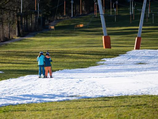Wintersportler fahren am Draxlhang im Skigebiet Brauneck mit einem Schlepplift die Piste hinauf. 