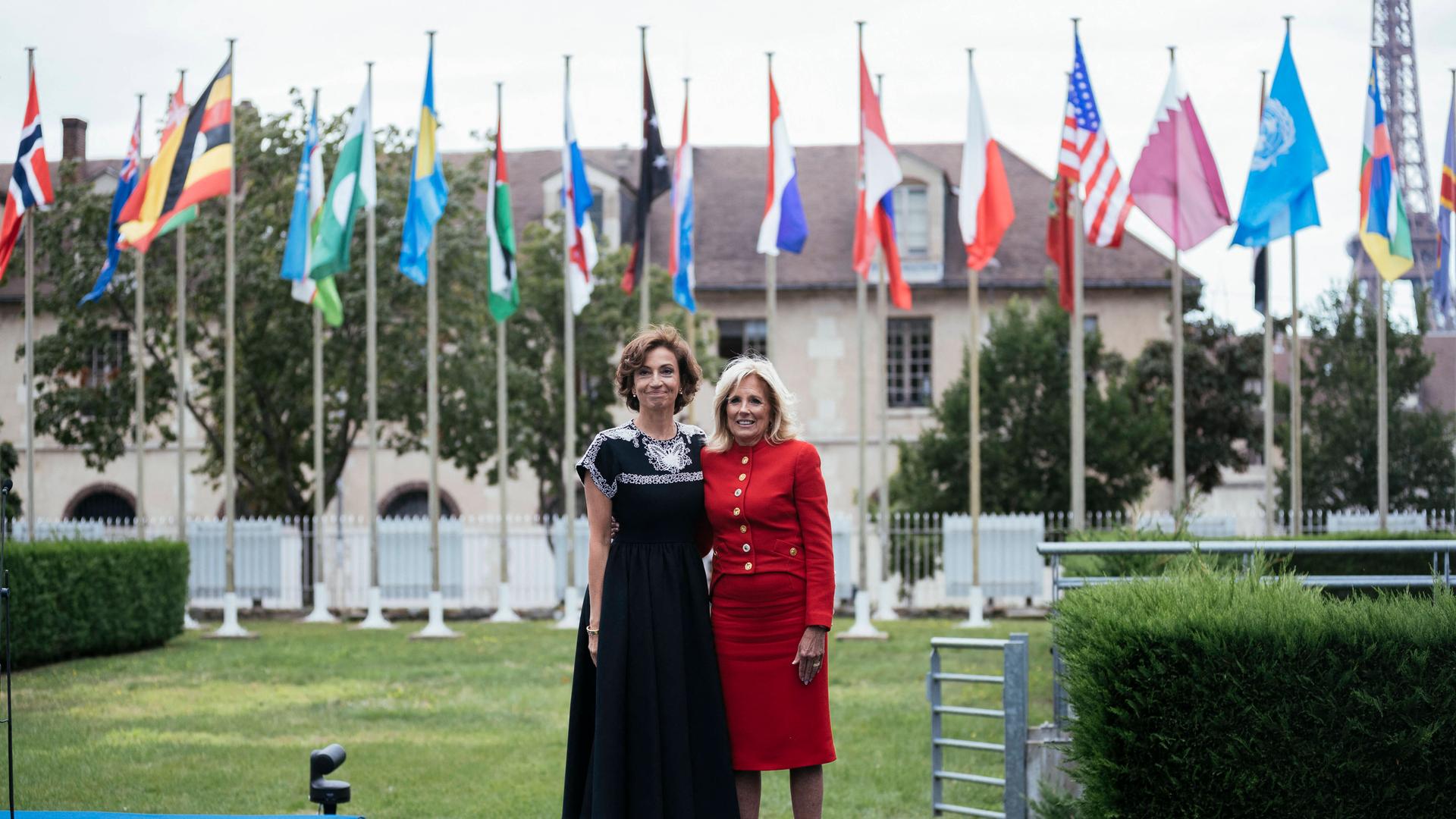 Die First Lady der USA, Jill Biden, und die Unesco-Generaldirektorin Audrey Azoulay stehen auf dem Gelände der Unesco in Paris. Im Hintergrund die Flaggen der Mitgliedsländer.