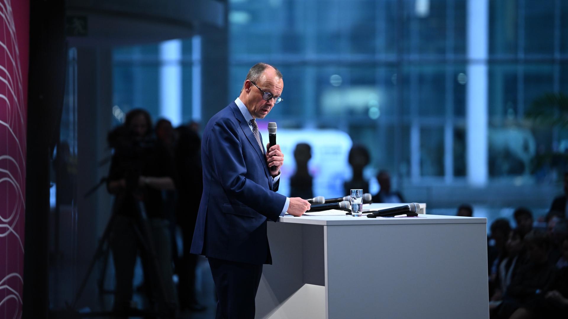 Friedrich Merz, CDU Bundesvorsitzender, steht im dunkelblauen Anzug an einem weißen Rednerpult, er hält ein Mikrofon in der Hand.