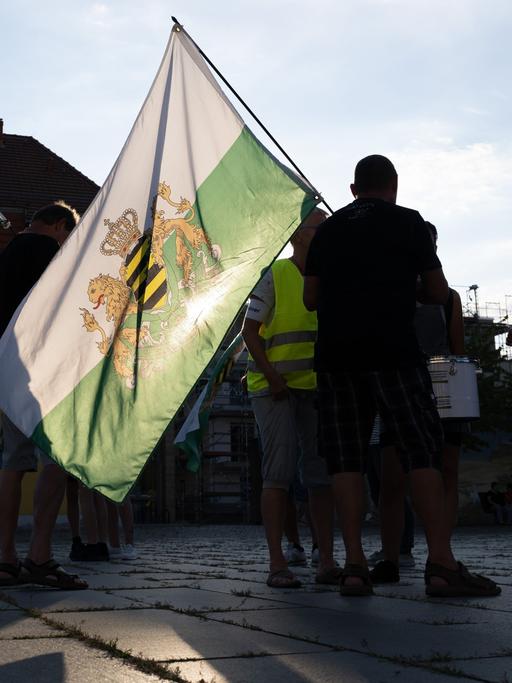 Teilnehmer einer Kundgebung der rechtsextremen Kleinstpartei "Freie Sachsen" stehen mit einer Fahne des einstigen Königreiches Sachsen auf einem Markplatz