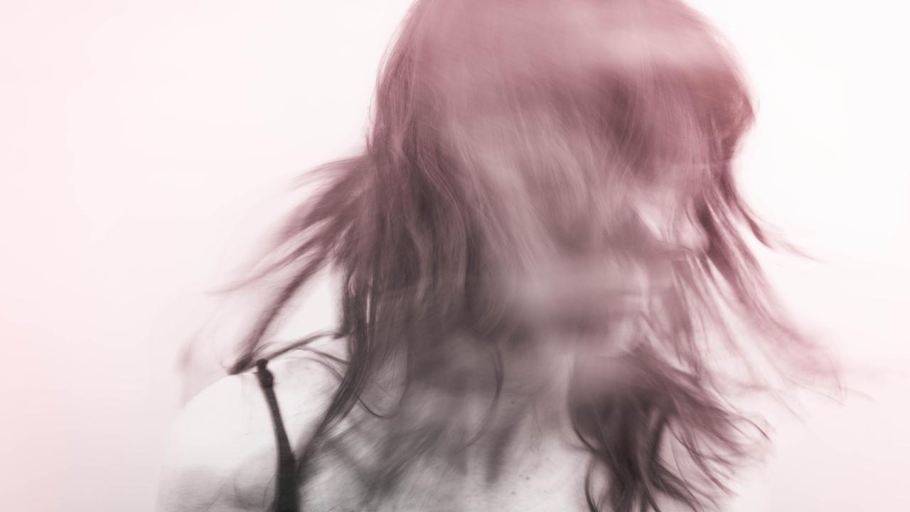 Verwischtes Bild einer Person, die den Kopf schüttelt und zur Seite schaut. Der Hintergrund ist weißlich. Die Person rötlich-violett.