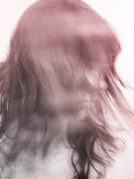 Verwischtes Bild einer Person, die den Kopf schüttelt und zur Seite schaut. Der Hintergrund ist weißlich. Die Person rötlich-violet.