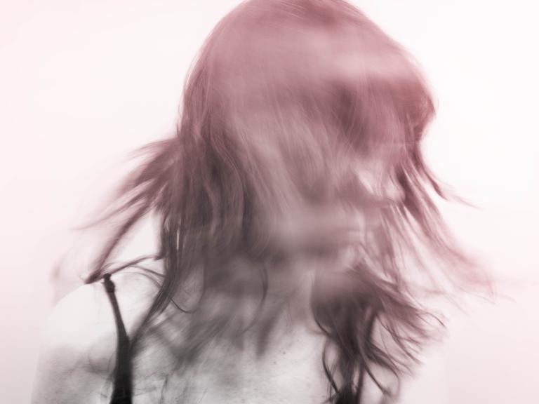 Verwischtes Bild einer Person, die den Kopf schüttelt und zur Seite schaut. Der Hintergrund ist weißlich. Die Person rötlich-violet.