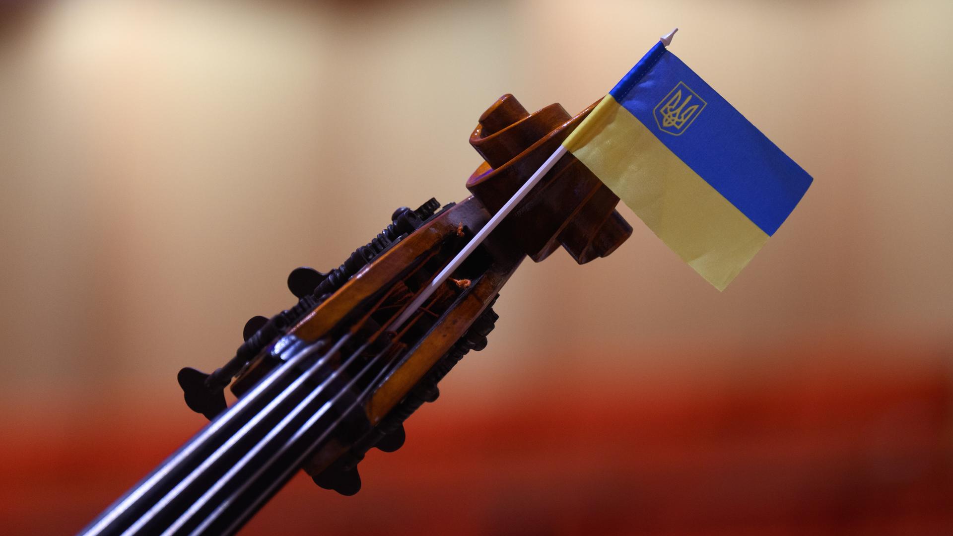 Wir sehen eine Geige, an deren Steg eine Ukraine-Flagge befestigt wurde. Wir sehen eine Geige, an deren Steg eine Ukraine-Flagge befestigt wurde.