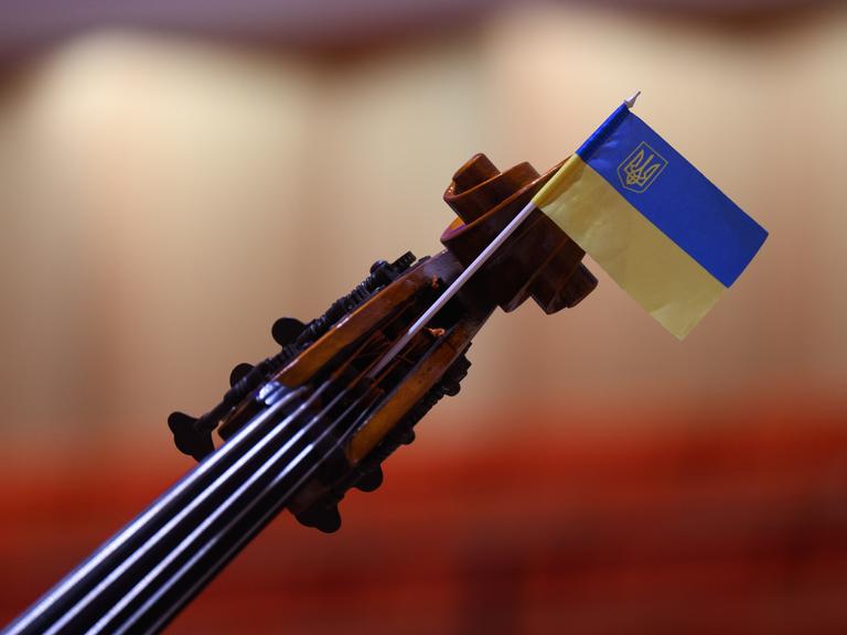 Wir sehen eine Geige, an deren Steg eine Ukraine-Flagge befestigt wurde. 