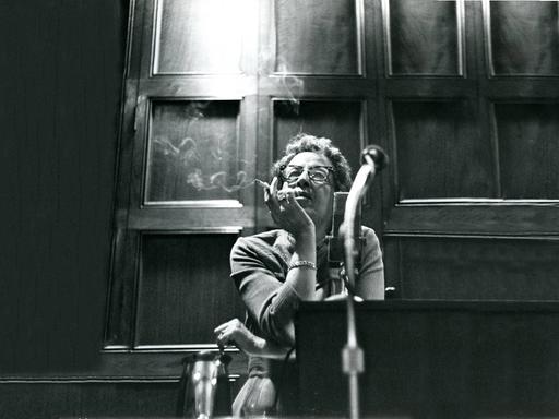Filmstill aus "Hannah Arendt - Die Pflicht zum Ungehorsam" in dem Hannah Arendt Zigarette rauchend sitzend an einem Tisch lehnt. 