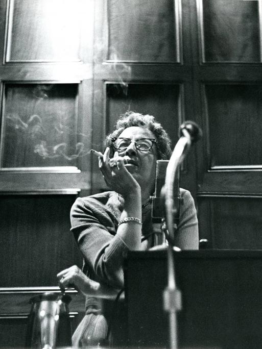Filmstill aus "Hannah Arendt - Die Pflicht zum Ungehorsam" in dem Hannah Arendt Zigarette rauchend sitzend an einem Tisch lehnt. 