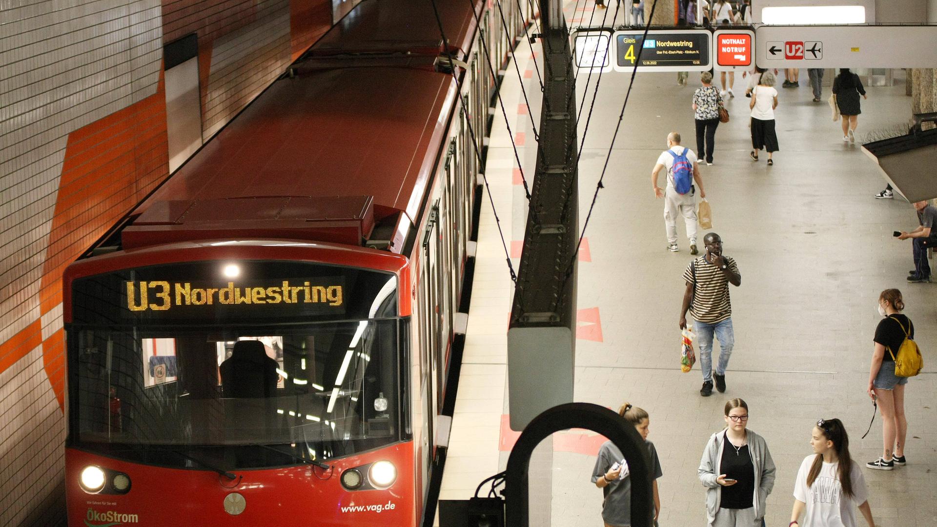 Zu sehen ist ein U-Bahnhof. Eine Bahn steht in der Haltestelle, Menschen laufen auf dem Bahnsteig herum.