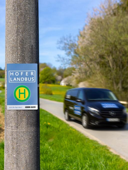 Ein Haltestellenschild mit der Beschriftung "Hofer Landbus", daneben ein Auto in Bewegung