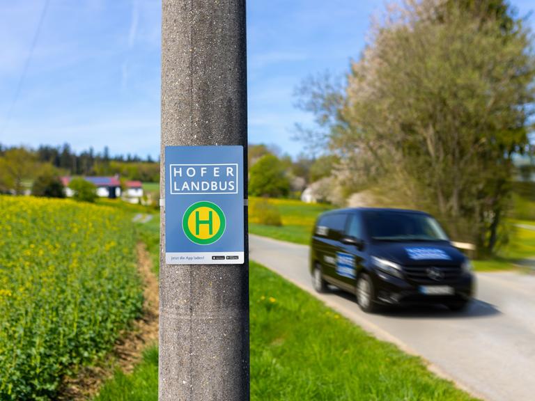 Ein Haltestellenschild mit der Beschriftung "Hofer Landbus", daneben ein Auto in Bewegung