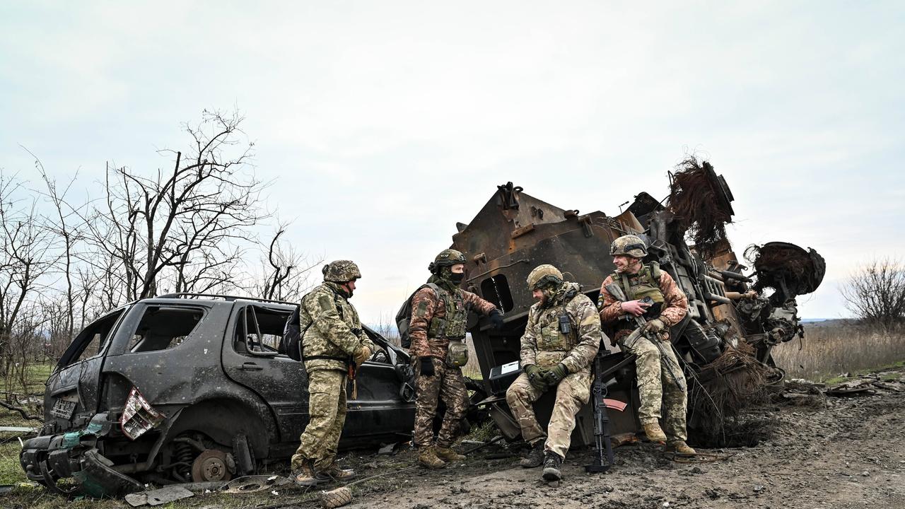 Soldaten der Ukraine machen eine Pause in der Region Saporischschja. Sie lehnen bewaffnet und im Tarnanzug an zwei ausgebrannten Fahrzeugwracks.   