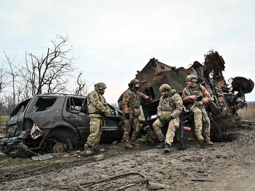 Soldaten der Ukraine machen eine Pause in der Region Saporischschja. Sie lehnen bewaffnet und im Tarnanzug an zwei ausgebrannten Fahrzeugwracks.   