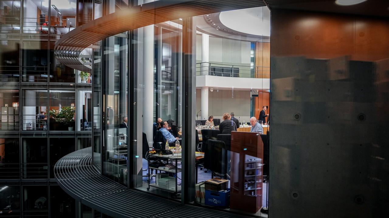 Abgeordnete und Helfer nehmen an der Haushaltsbereinigungssitzung im Paul-Löbe-Haus teil. Durch eine große Fensterfront sind die Menschen an Schreibtischen zu erkennen, draußen ist es dunkel. 