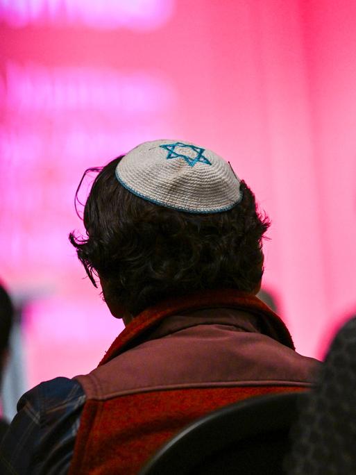 Ein Mann mit einer Kippa, auf die der Davidstern zu sehen ist, sitzt zwischen anderen Menschen. Der Mann ist von hinten zu sehen.