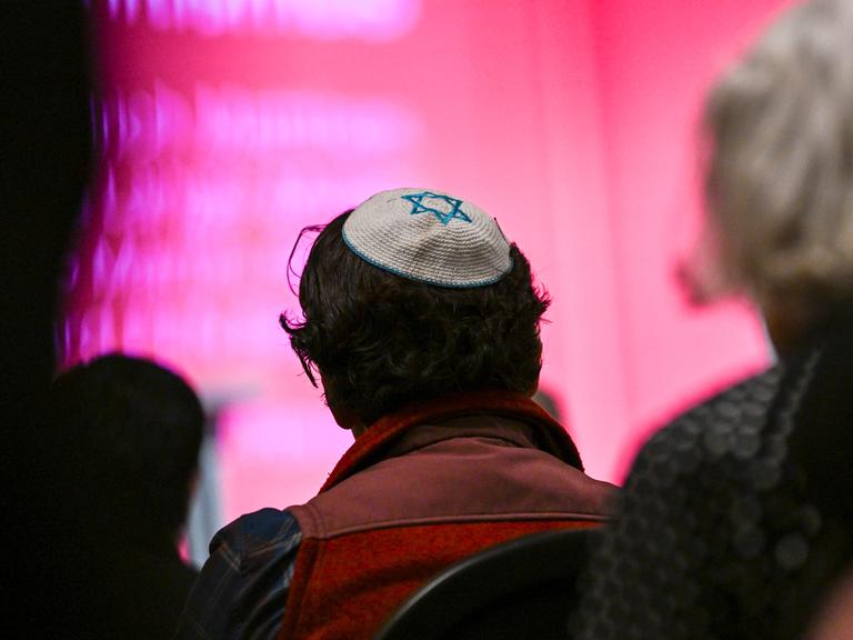 Ein Mann mit einer Kippa, auf die der Davidstern zu sehen ist, sitzt zwischen anderen Menschen. Der Mann ist von hinten zu sehen.